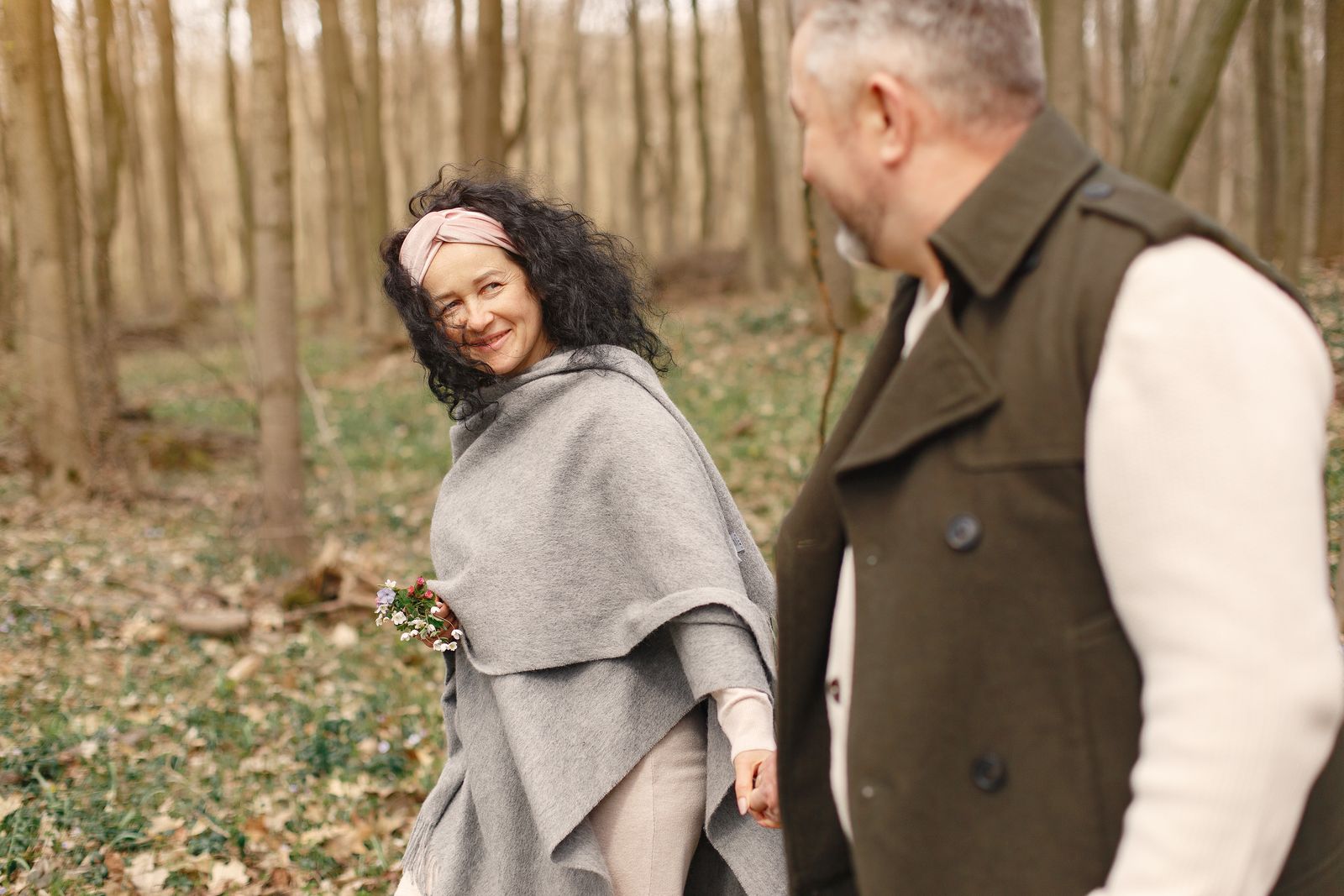 Un couple marche main dans la main dans une forêt de printemps, la femme sourit en se retournant.