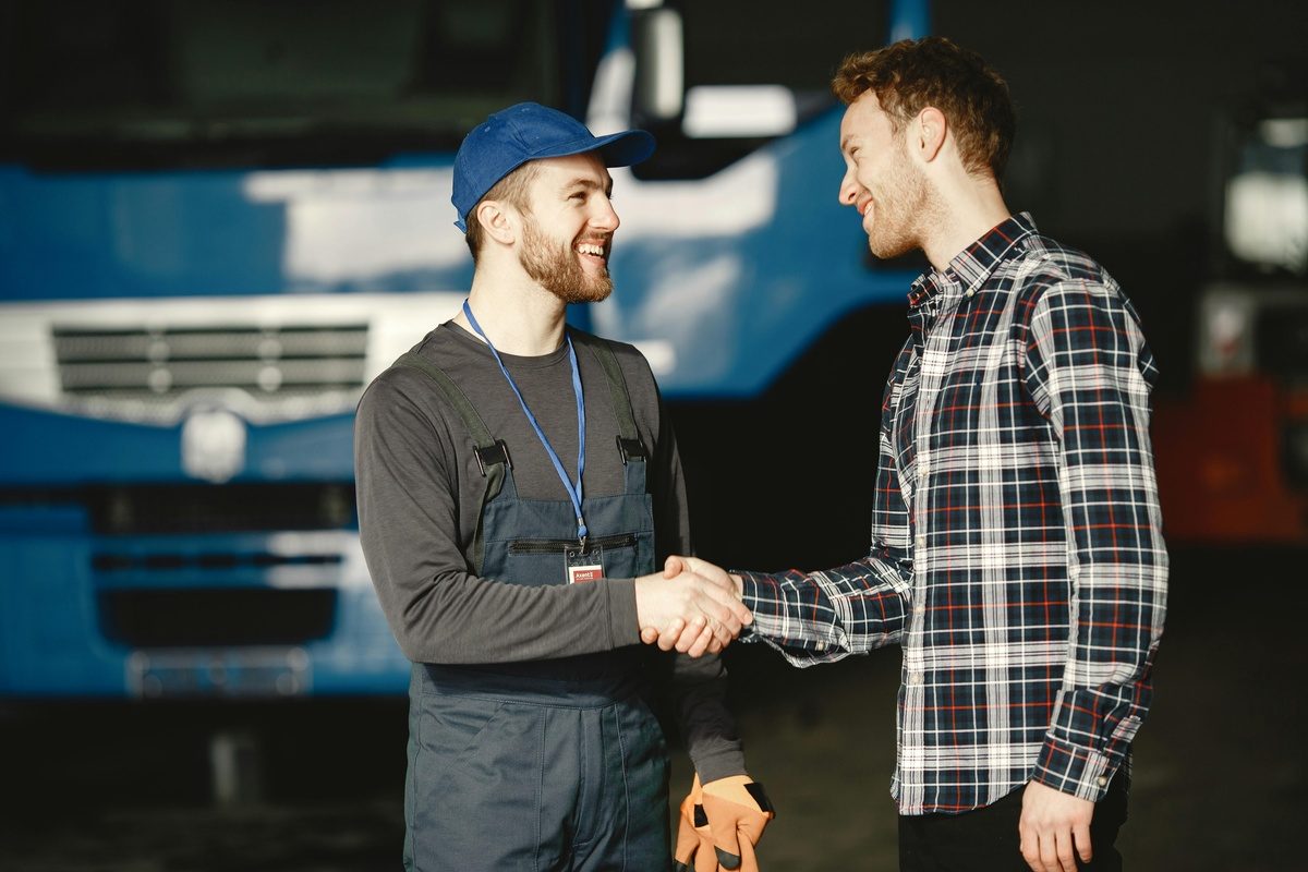 Mechanic in branded uniform and customer shaking hands in front of a truck