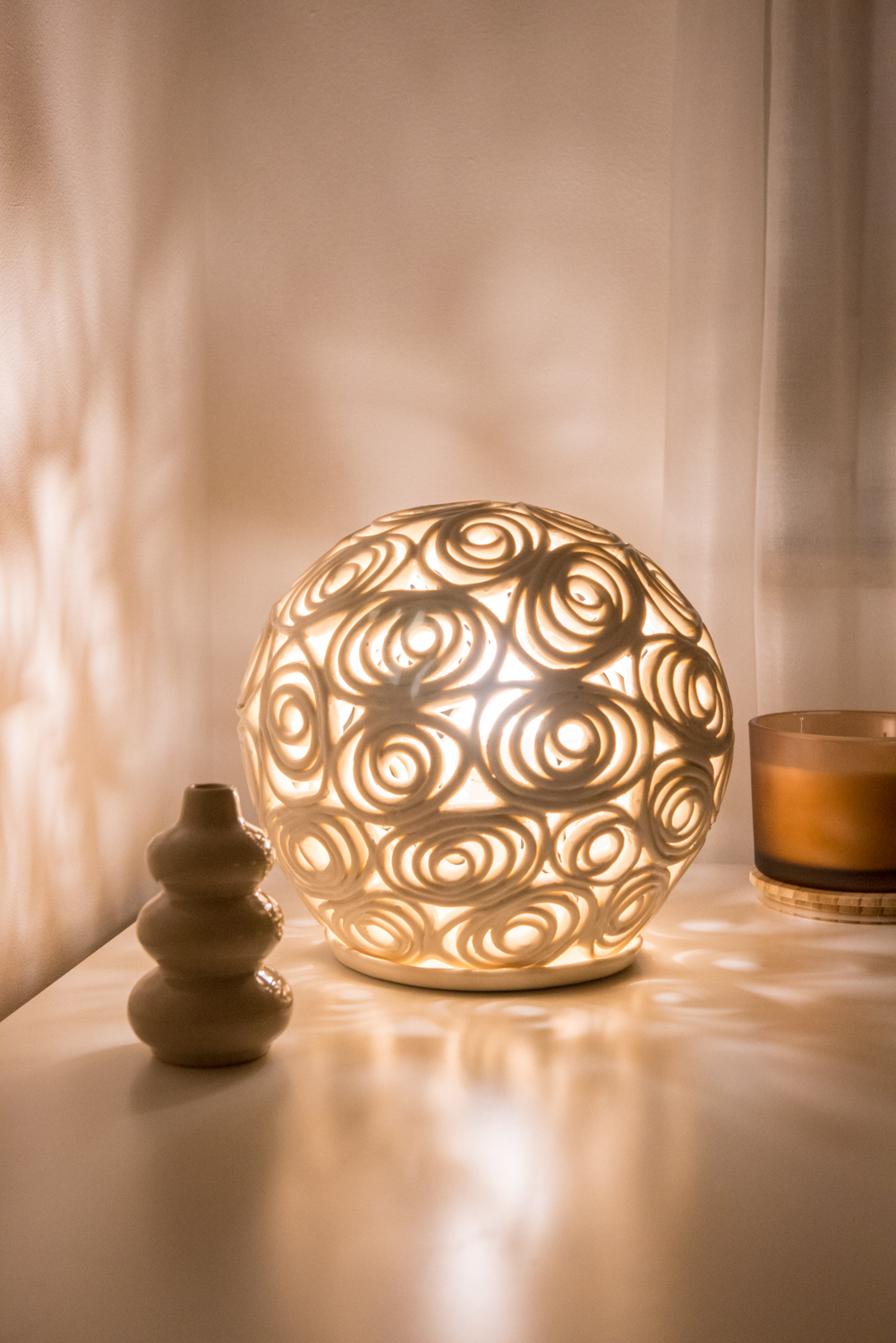Sculptural glowing bedside lamp with a small ceramic vase and candle