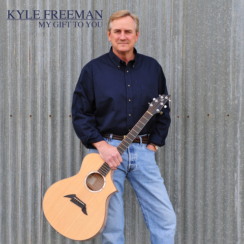 Album cover for My Gift to You by Kyle Freeman featuring Kyle standing with an acoustic guitar against corrugated metal