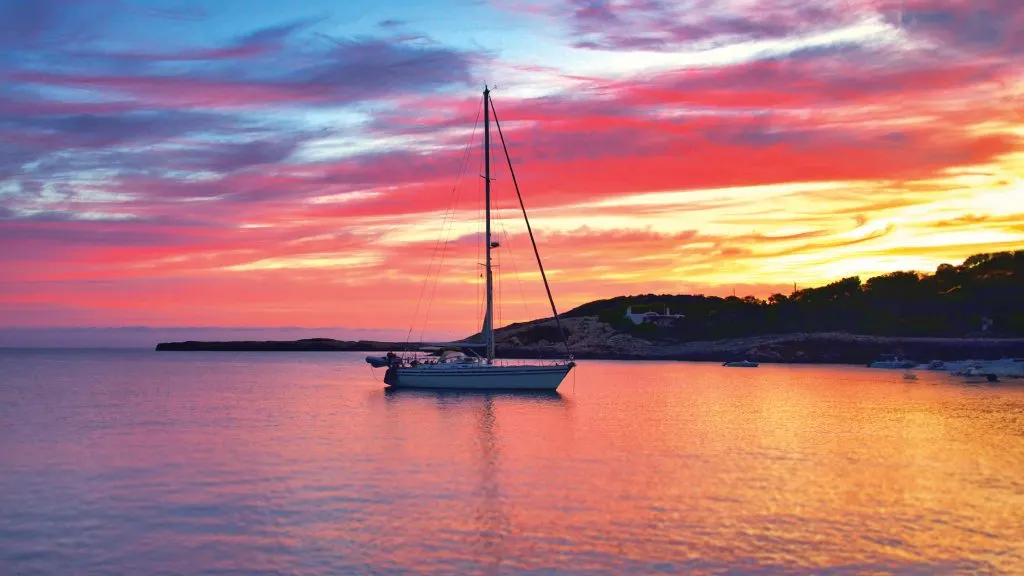 Un voilier au mouillage au coucher du soleil, avec le ciel rose et orange