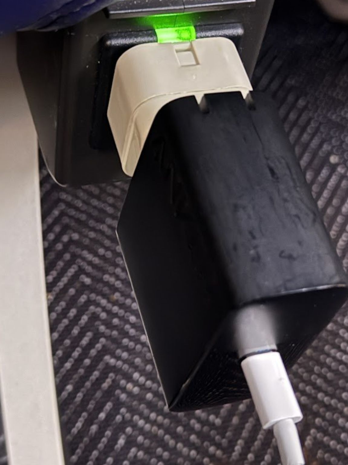 A travel adapter plugged into an airplane power outlet with a laptop charger plugged into the adapter