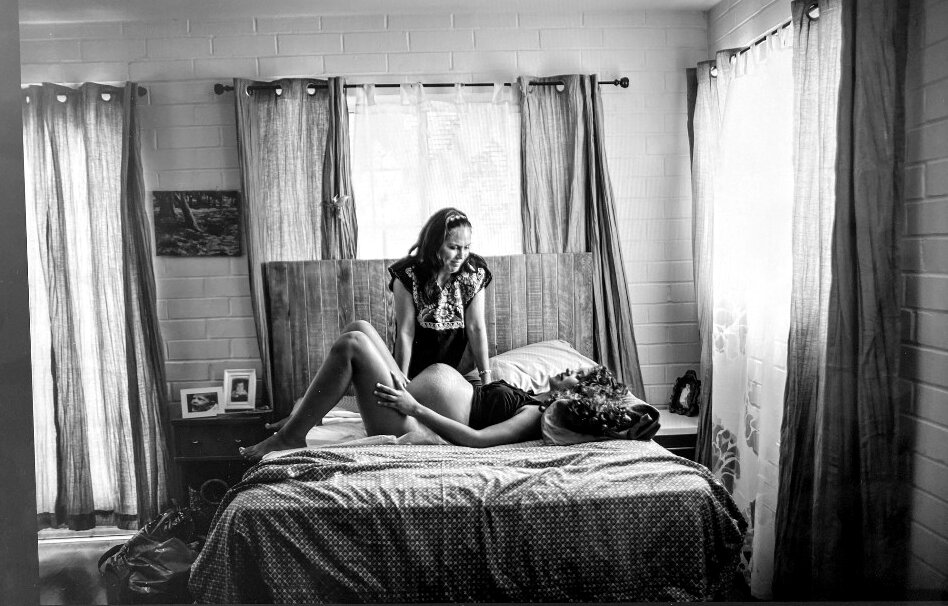 A midwife sits at the bedside supporting a laboring mother at home
