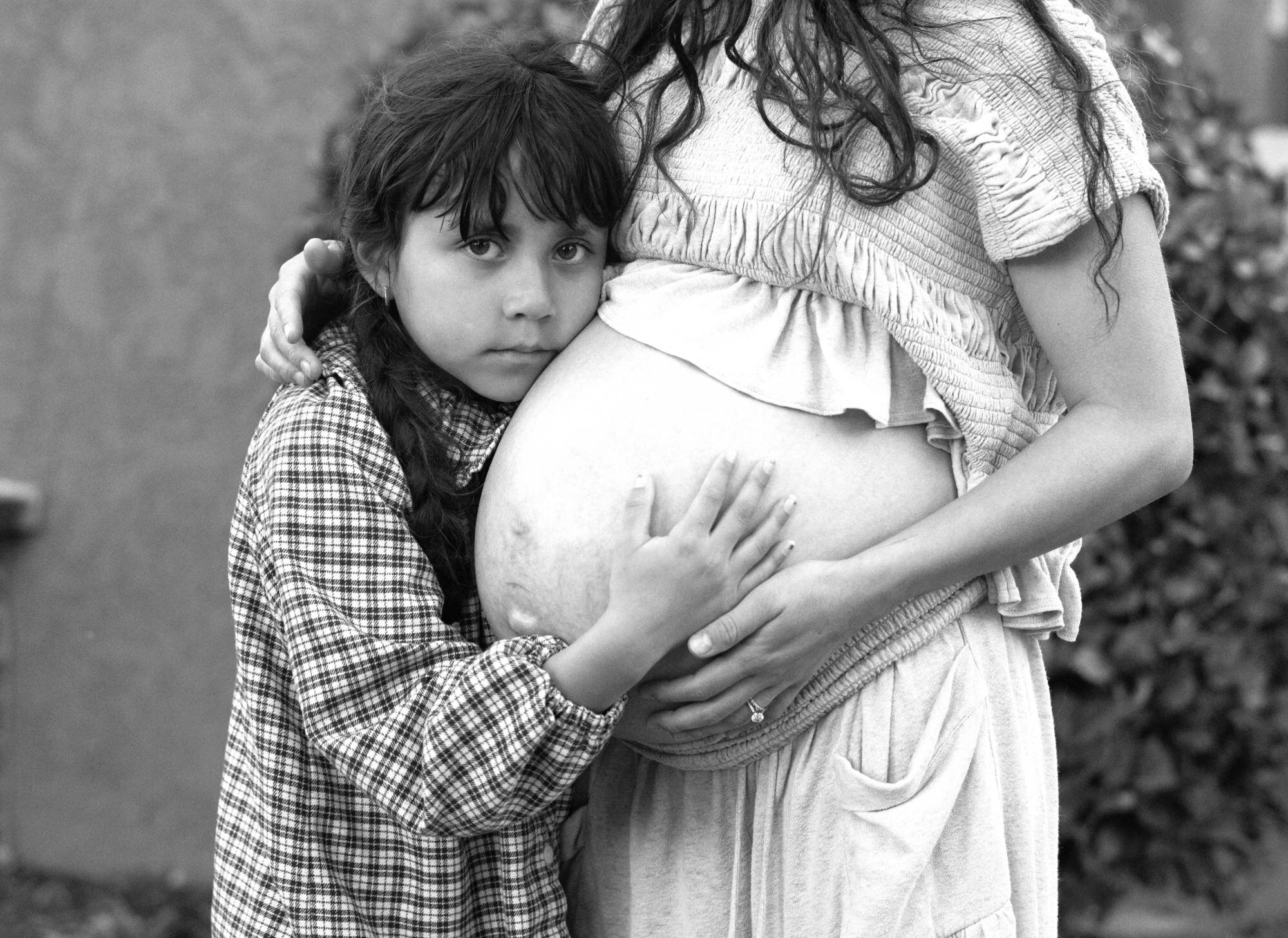 A young girl presses her cheek to her mother's pregnant belly