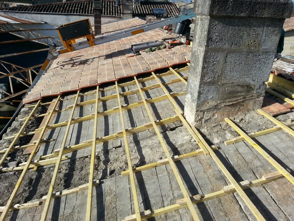 Chantier de couverture avec des liteaux en bois apparents et des tuiles en cours de pose autour d’une cheminée