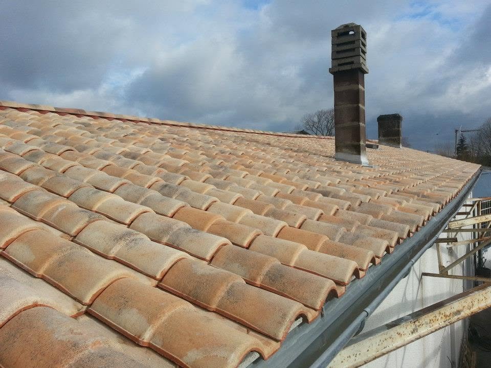 Vue d’une toiture en tuiles de terre cuite avec une cheminée et une gouttière en bord de couverture