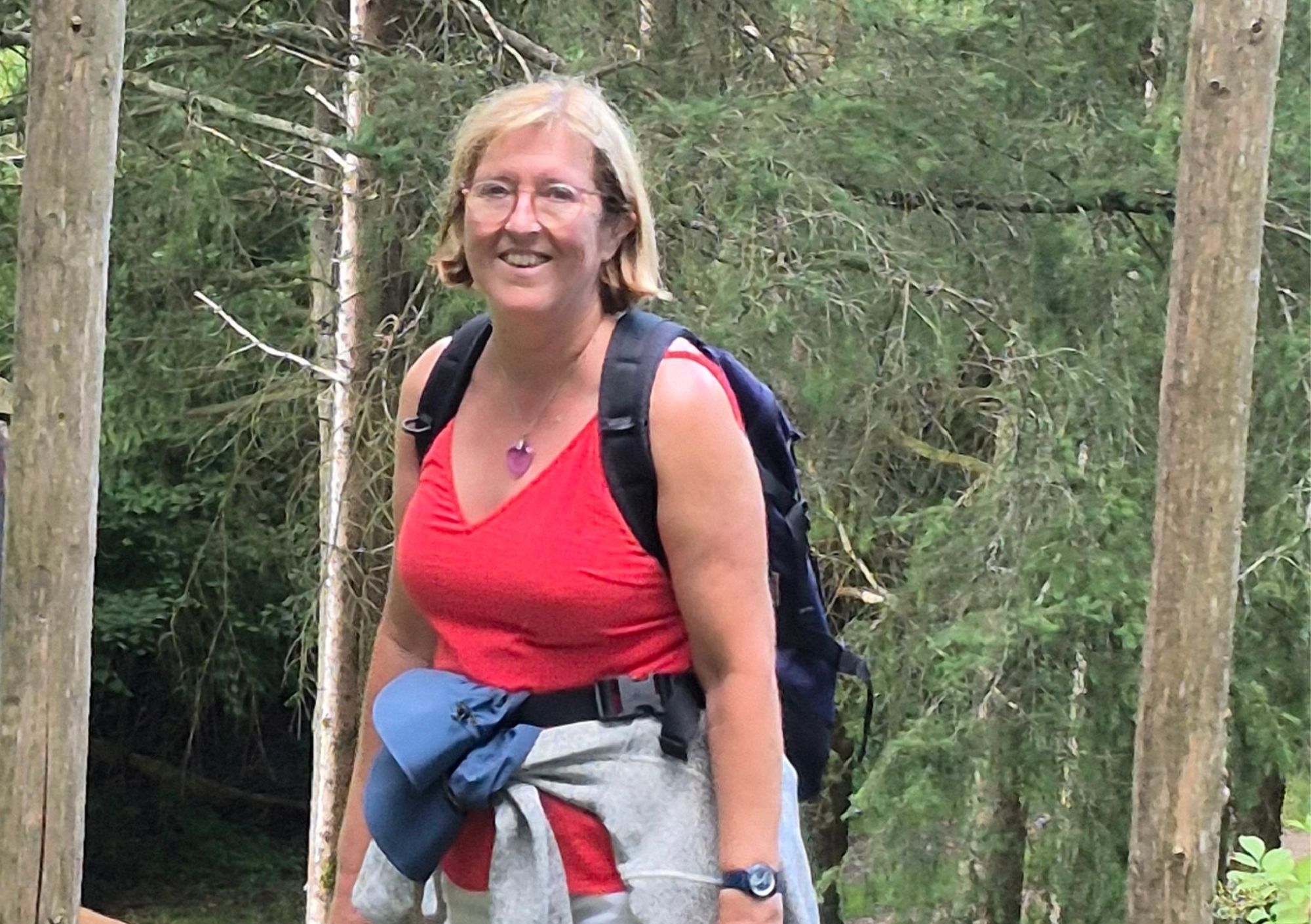 Christine lacht tijdens een wandeling in het bos, met rugzak