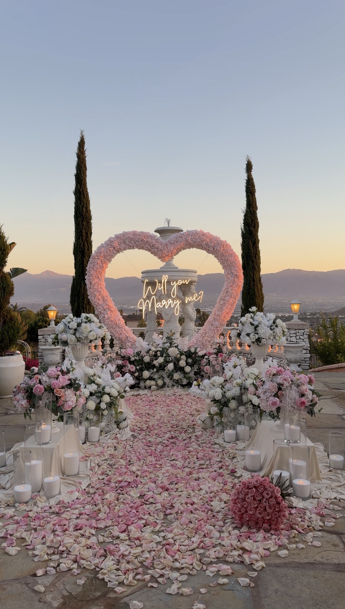 Marriage proposal beneath a pink heart-shaped floral arch with rose petals and romantic decor