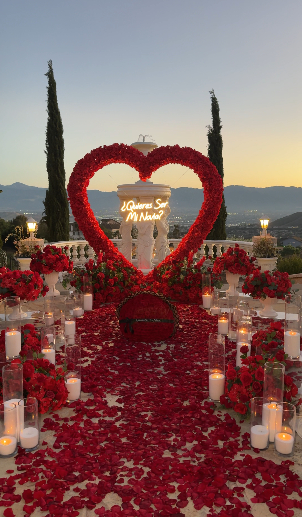 Marriage proposal beneath a red heart-shaped floral arch with rose petals and romantic decor