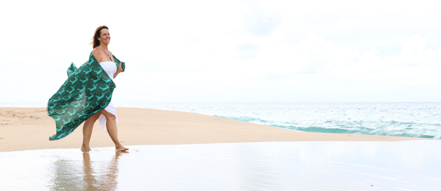 Wanda standing by the ocean with a turquoise scarf outstretched in the breeze