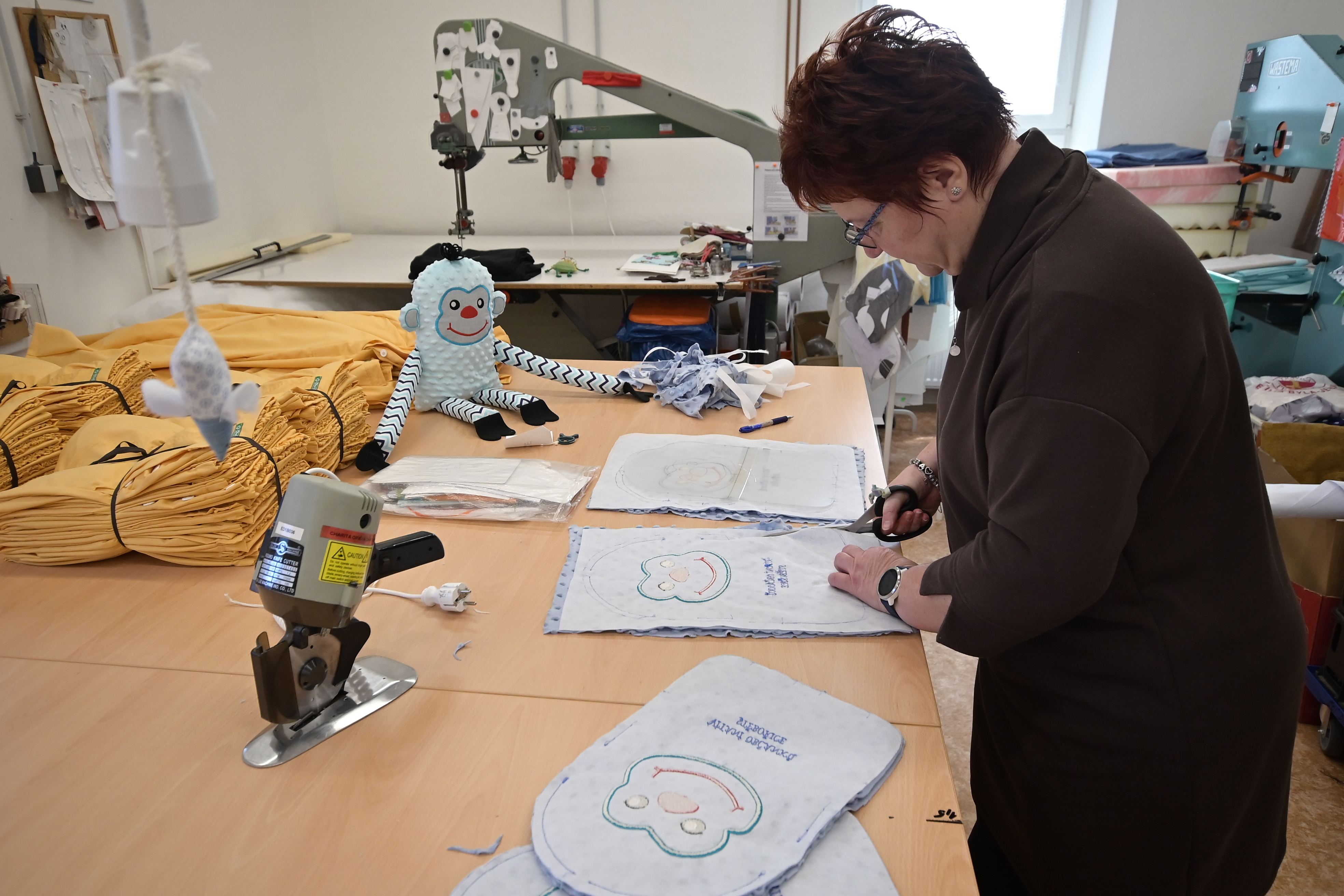 Mistrová šicí dílny pracuje na střihárně na přípravě dětských polštářků. 
