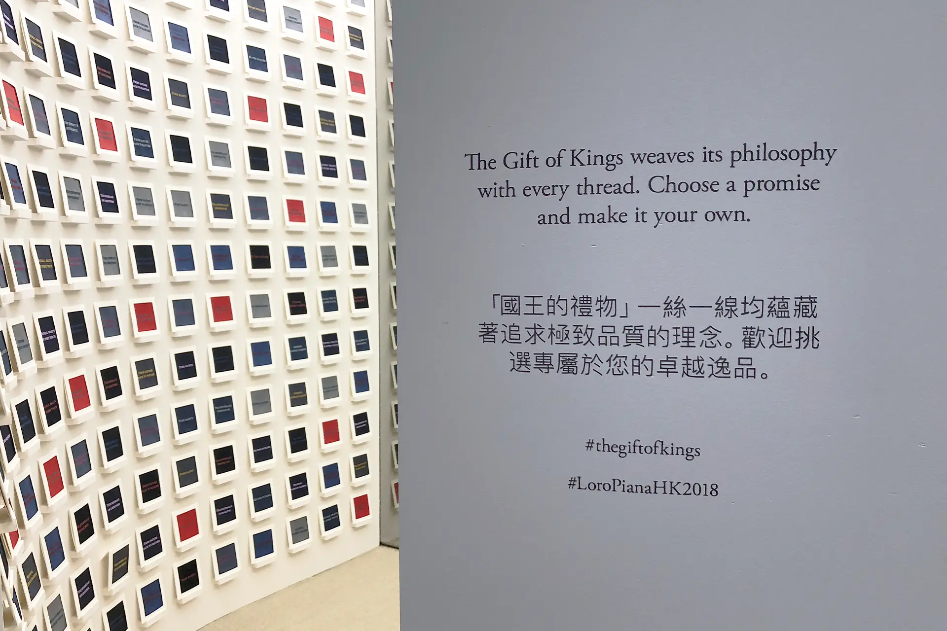 An installation wall displaying hundreds of small framed text cards arranged in a grid, alongside a panel of exhibition text describing The Gift of Kings philosophy in English and Chinese.