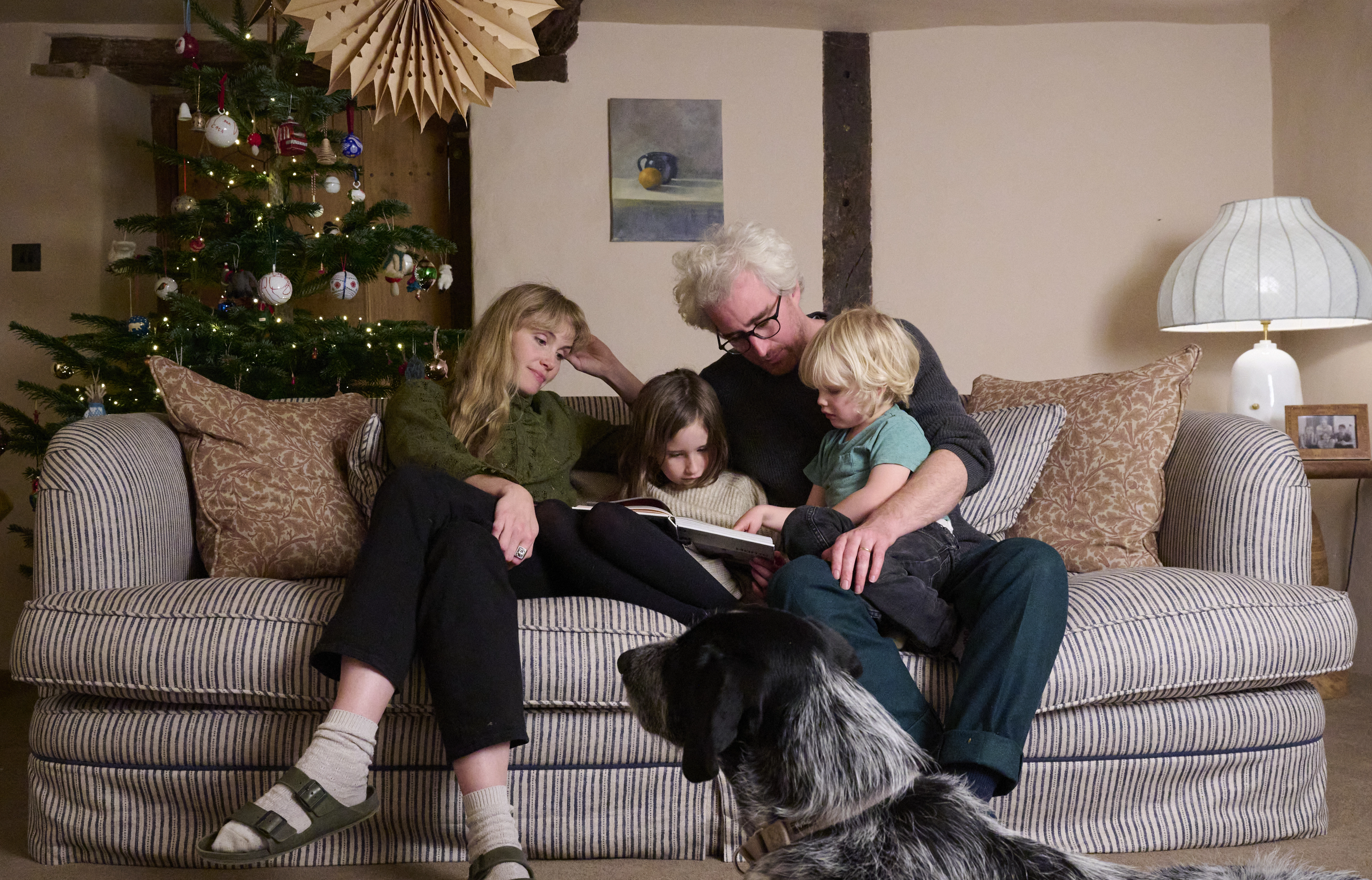 A family sits together on a sofa reading, with a Christmas tree nearby.