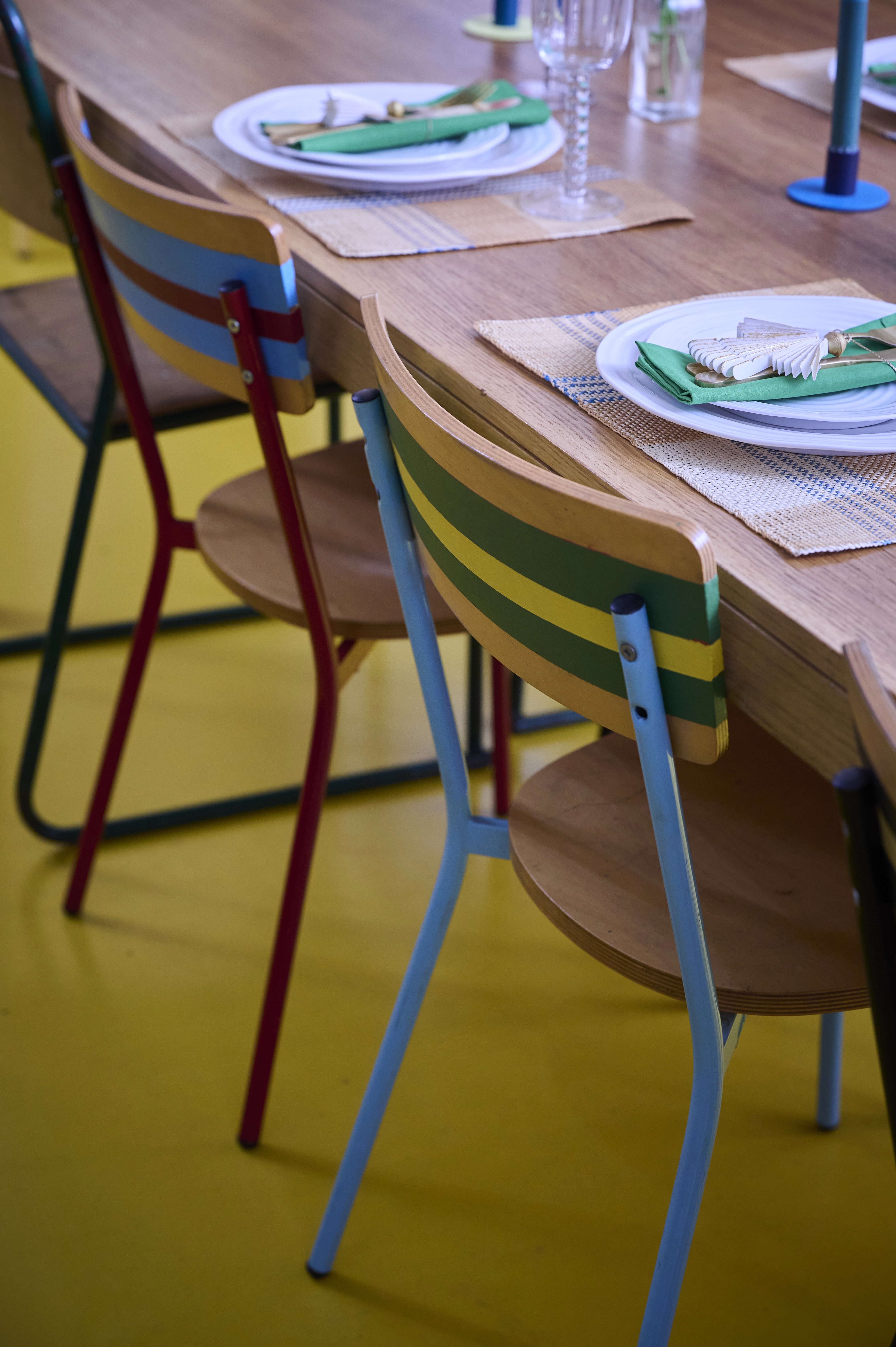 A wooden dining table with colourful chairs and place settings.