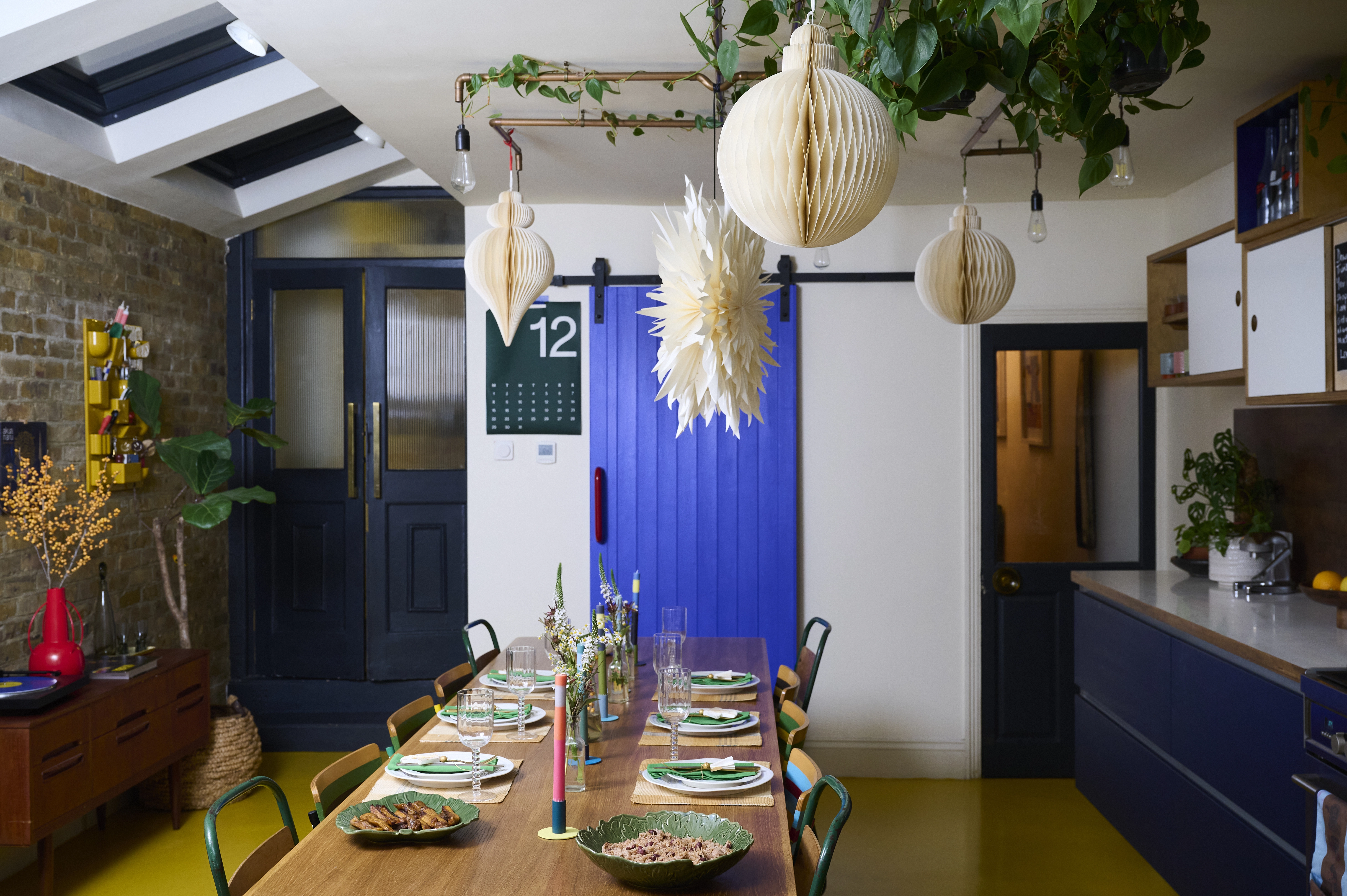 A long dining table set with plates and candles in a bright, colourful kitchen.