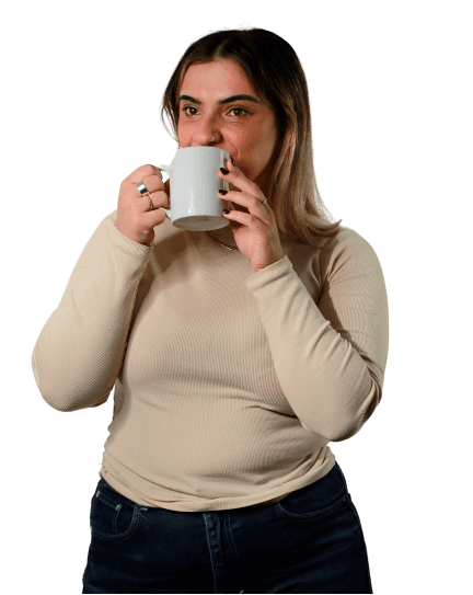 Chiara is wearing black jeans and a beige long-sleeved t-shirt as she looks off-camera while sipping from a white coffee mug.
