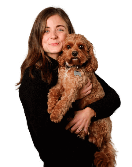 Danielle is wearing a black jumper and blue jeans as she hugs her small brown dog and smiles into the camera.