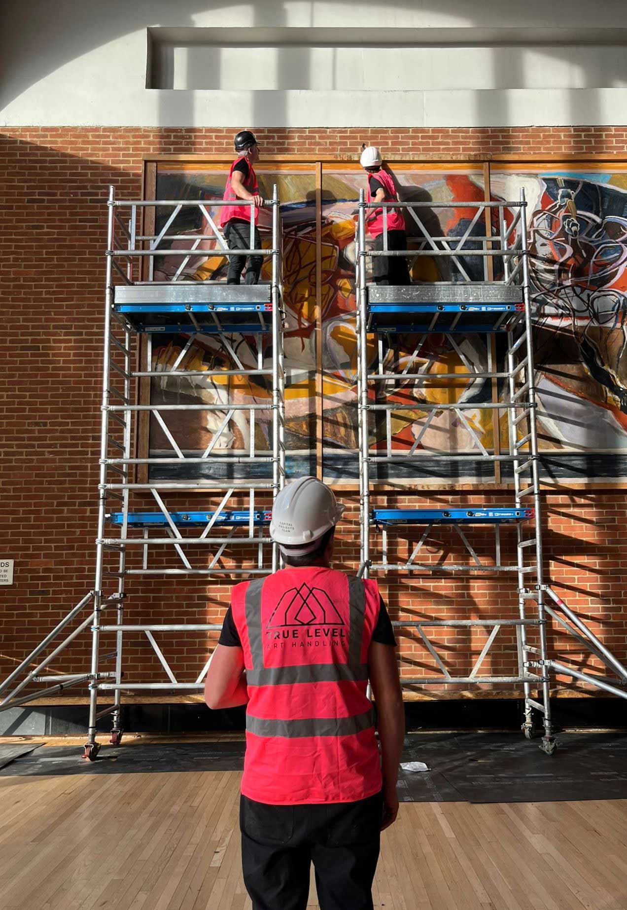 True Level employees carefully installing a large art piece on safety platforms