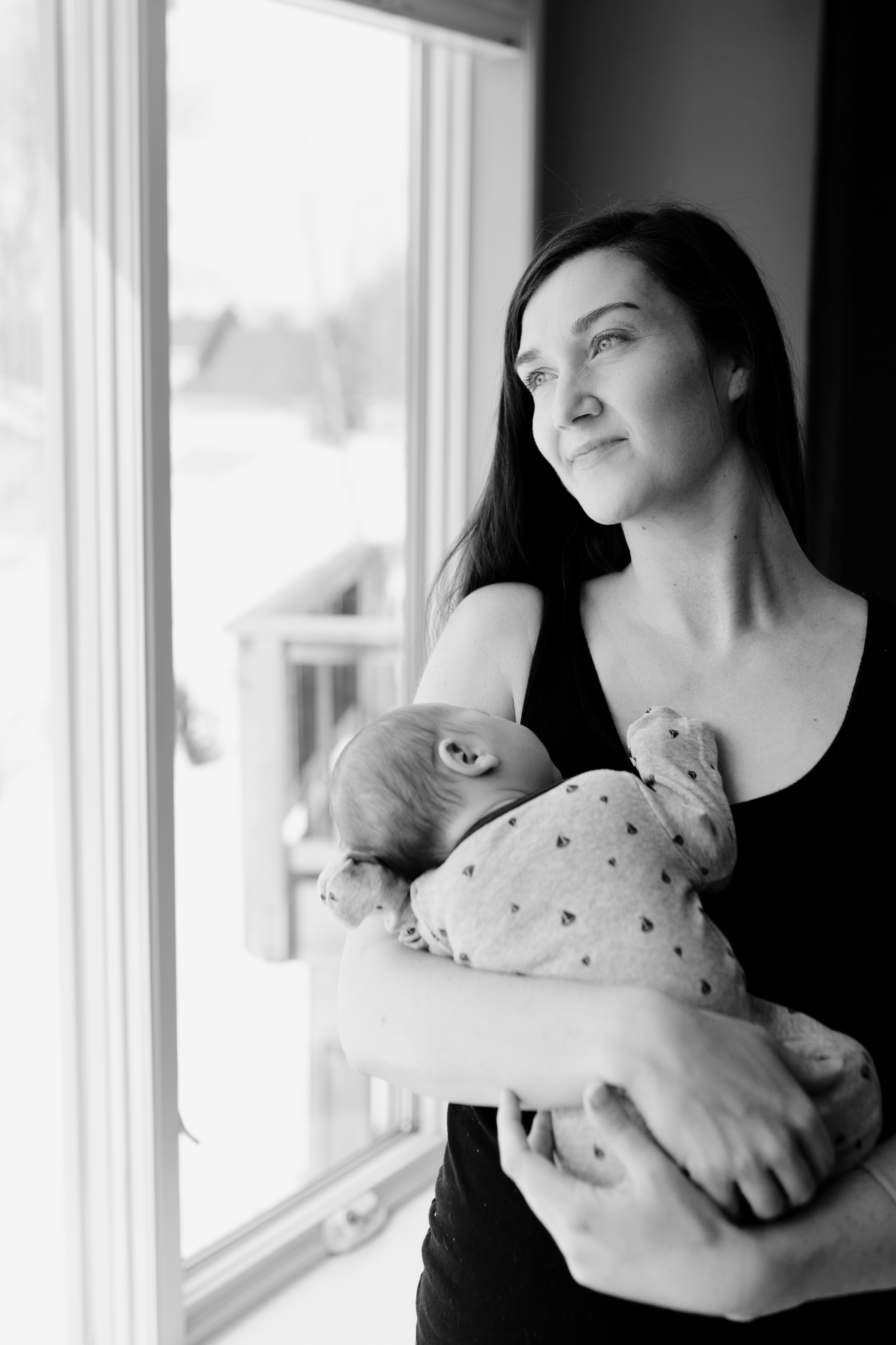 Jenna Hedlund holding newborn son looking out a bay window